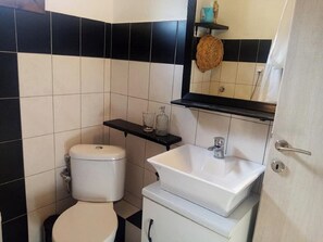 A bathroom with a toilet, sink, and mirror. There is a shelf with toiletries.