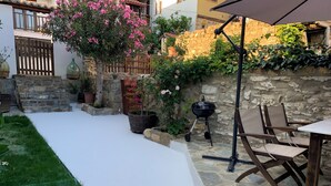 A patio area with a stone wall, a wooden table, and chairs. There is a grill and potted plants. - Beautiful Petrino 1880 (Sithonia)