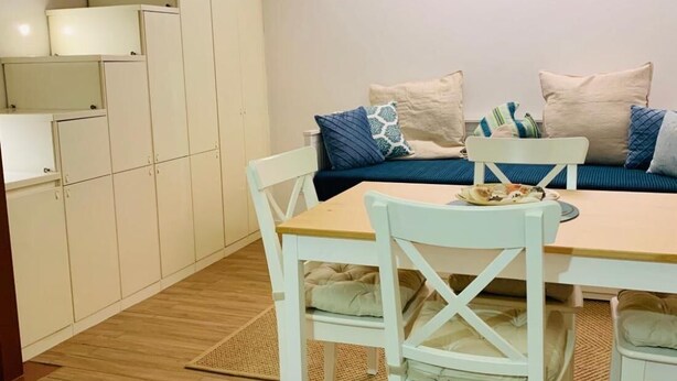 Um quarto acolhedor com uma mesa de jantar, cadeiras, um sofá com almofadas e um conjunto de armários.
