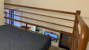 Quarto com cama, cabeceira de madeira e televisão fixada na parede.