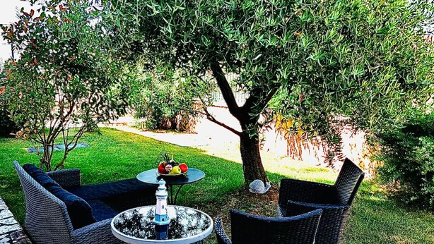 An outdoor seating area with wicker furniture and a round table, surrounded by a well-maintained lawn and trees. - Vip Luxurious Apartment (Medulin)