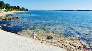 A clear beach with rocky shoreline, calm water, and a distant landmass. - Vip Luxurious Apartment (Medulin)