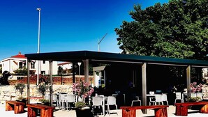 An outdoor café with wooden benches and tables, surrounded by stone walls and potted plants. - Vip Luxurious Apartment (Medulin)
