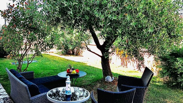An outdoor seating area with wicker furniture and a round table, surrounded by a well-maintained lawn and trees. - Vip Luxurious Apartment (Medulin)