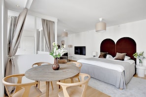 A modern hotel room with a bed, bedside table, lamp, and a round dining table with chairs.