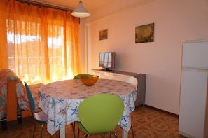 Cozy living space with a dining area, featuring a round table for two, a comfortable chair, and a refrigerator.