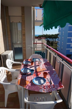 Un balcon avec une table dressée pour quatre personnes, des chaises en plastique blanches et un auvent vert.
