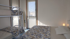 A room with bunk beds and a single bed, a window with curtains, and a wall-mounted light. - Vacation by the Beach-beahost (Caorle)