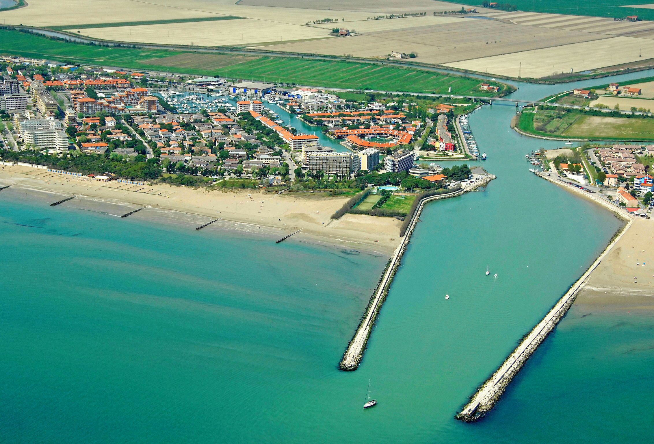 Vista aérea de uma cidade costeira com um porto de iates, praia e edifícios residenciais.