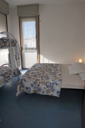 A room with bunk beds, a window with curtains, and a bed with a patterned blanket. - Luminous Flat by the sea (Caorle)