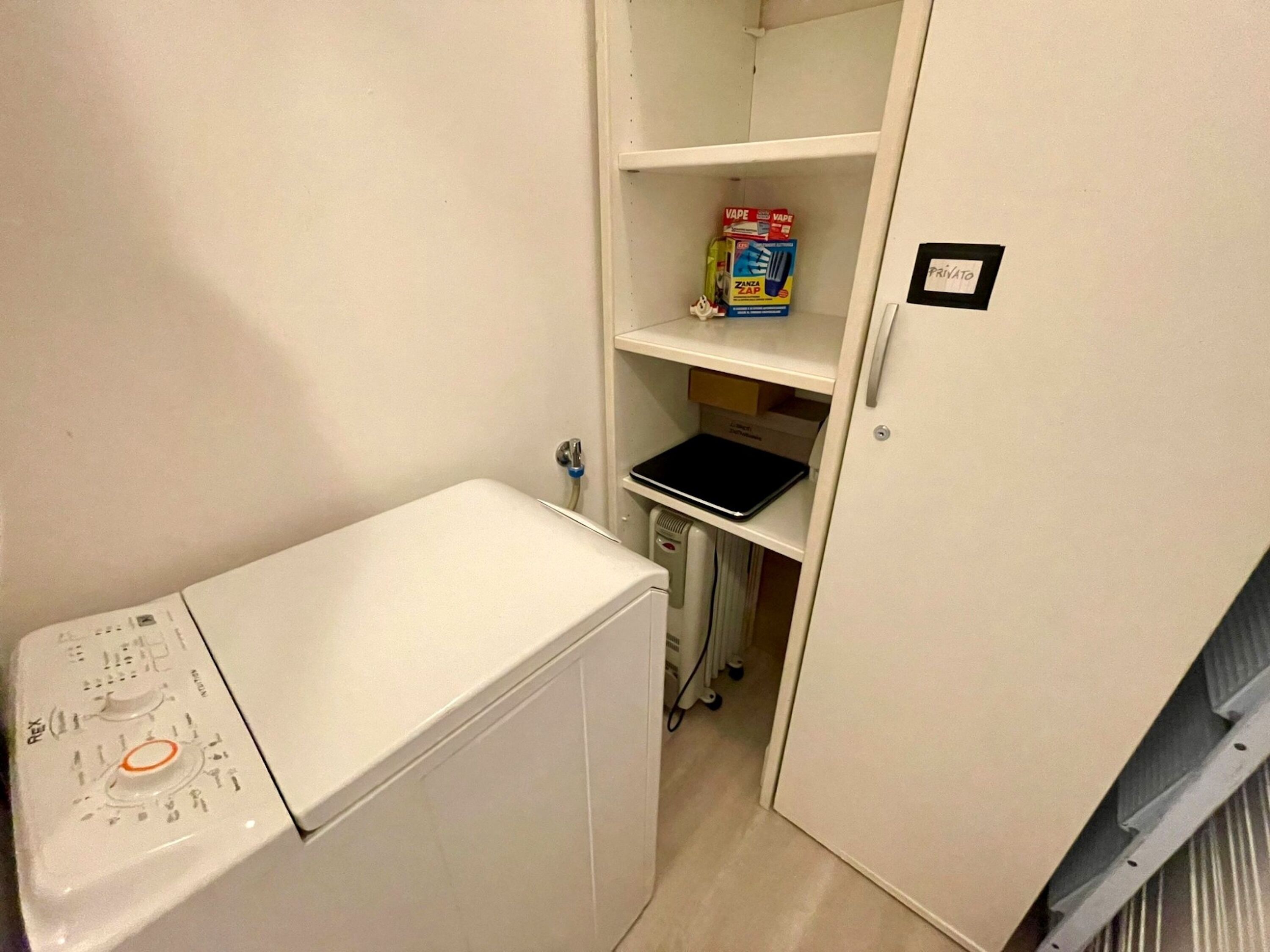 A compact room with a washing machine, a shelf with a box labeled "VAPE," and a small table.