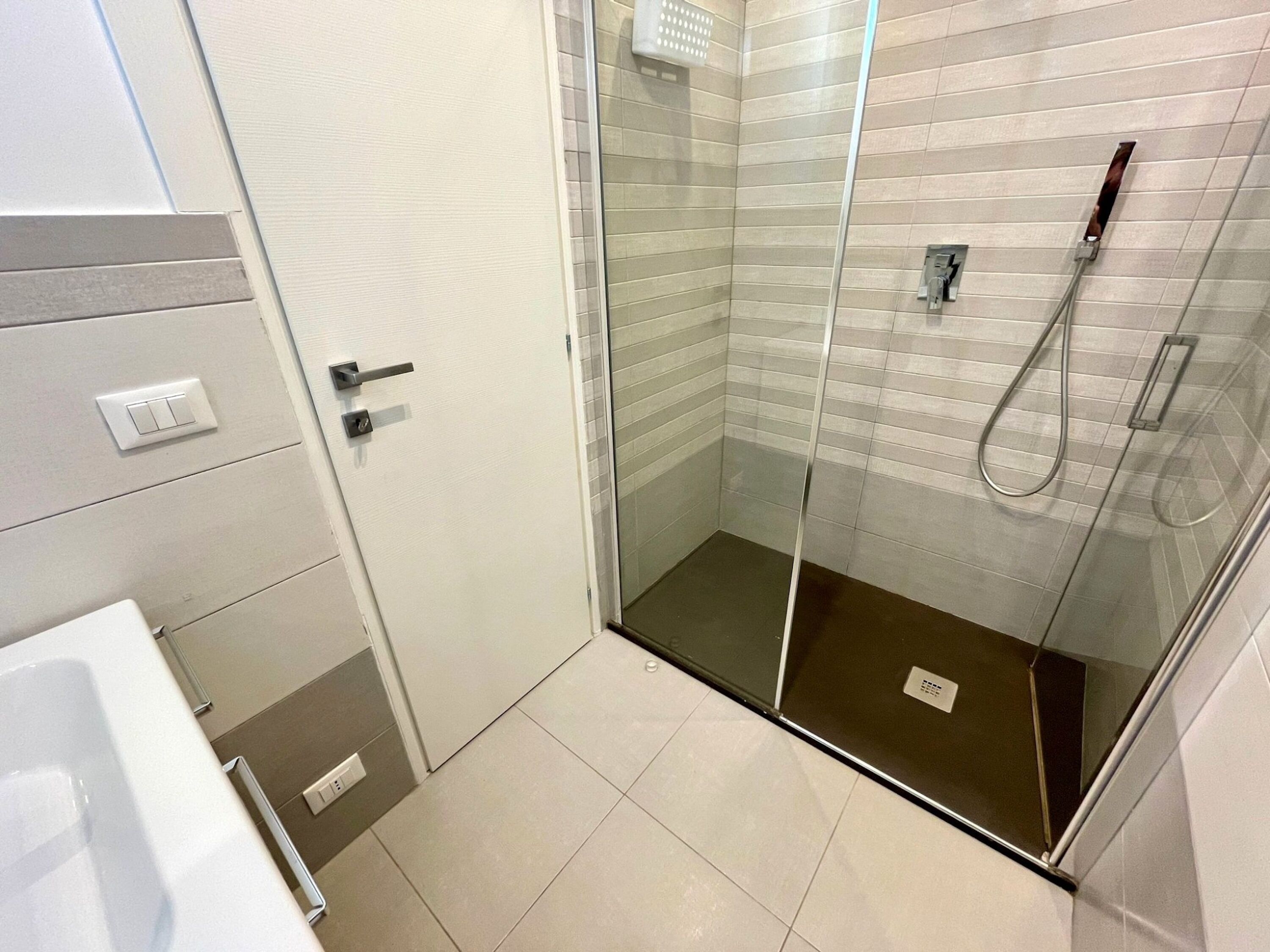 Une salle de bain moderne avec une douche à parois de verre, une porte blanche et un sol carrelé.