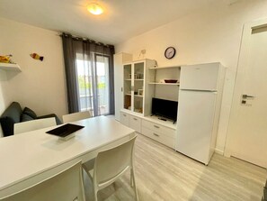 Una cucina compatta con un tavolo da pranzo, sedie, un frigorifero e una televisione.