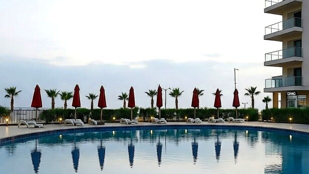 Ein Pool mit Liegestühlen und Sonnenschirmen, umgeben von Palmen und einem Gebäude mit Balkonen.