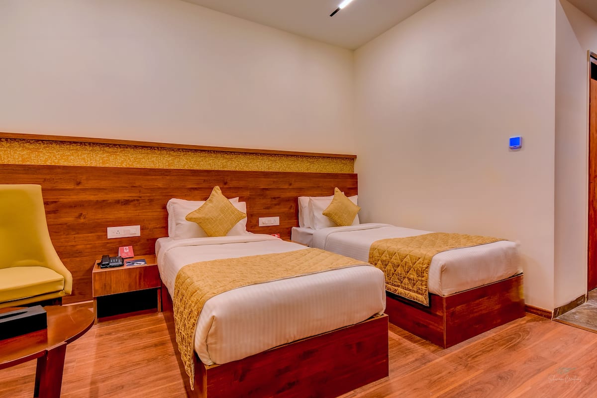 Une chambre d’hôtel avec deux lits, une tête de lit en bois, un fauteuil jaune, des tables de chevet et une petite table de nuit.