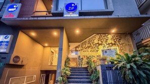 Entrada de hotel con escaleras, plantas en macetas y letreros que dicen 'Zip' y 'Sree Hotels'.