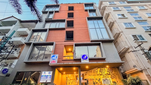 Un hotel de varios pisos con diseño moderno, que cuenta con balcones, una entrada a nivel de suelo con escaleras y señalización para servicios como Wi-Fi y un restaurante.