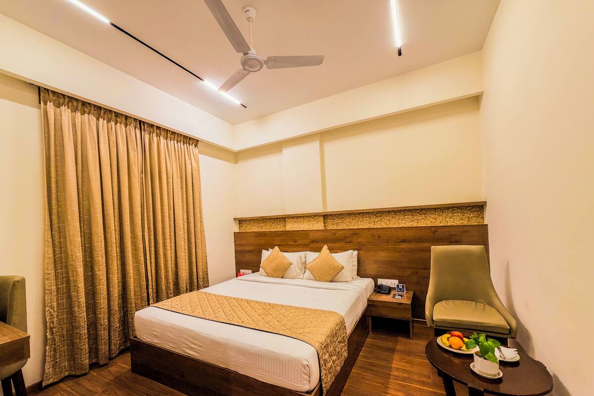 Une chambre d’hôtel avec un lit, une chaise, une petite table avec des fruits et un ventilateur de plafond.