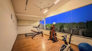 Un gimnasio moderno con equipo de ejercicio, un ventilador de techo y un ventanal con vistas a la vegetación.