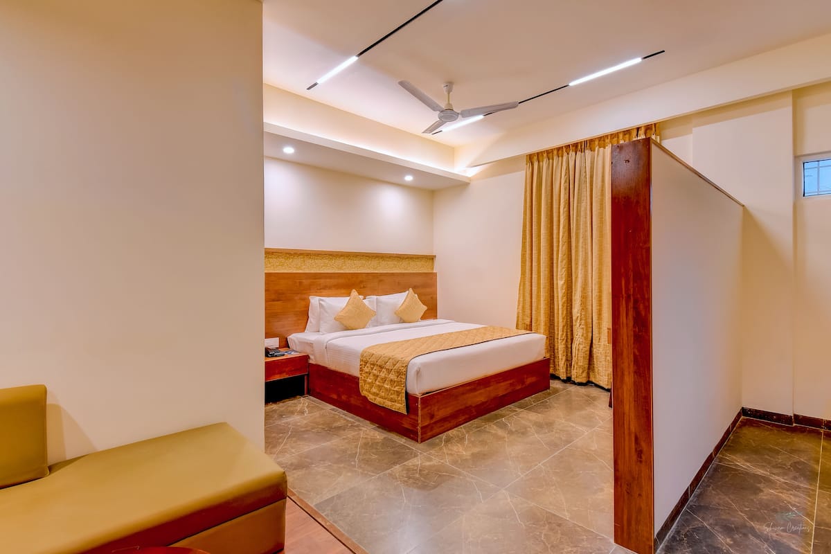 Une chambre d’hôtel moderne avec une tête de lit en bois, un lit recouvert d’une couverture beige, une table de chevet et un banc en bois.