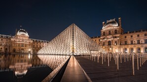La Pirámide del Louvre con su reflejo en el agua, rodeada de arquitectura clásica.