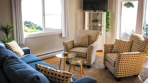 A living room with a blue sofa, patterned armchairs, a glass coffee table, and a TV mounted on the wall. - Bayside Apartment #4- Top Floor Waterfront Views above Boulevard Park (Bellingham)