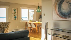A living room with a sofa, a dining table with chairs, and a view of the outdoors through a window. - Bayside Apartment #4- Top Floor Waterfront Views above Boulevard Park (Bellingham)