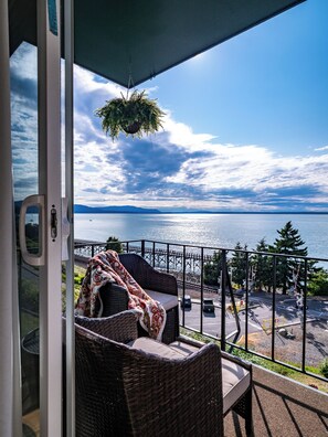 A balcony with wicker furniture, a hanging plant, and a view of the sea and mountains. - Bayside Apartment #4- Top Floor Waterfront Views above Boulevard Park (Bellingham)