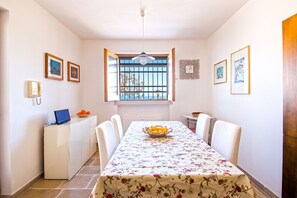 Un coin repas avec une table dressée pour quatre personnes, une fenêtre avec des barreaux, un téléphone et des tableaux encadrés accrochés aux murs.