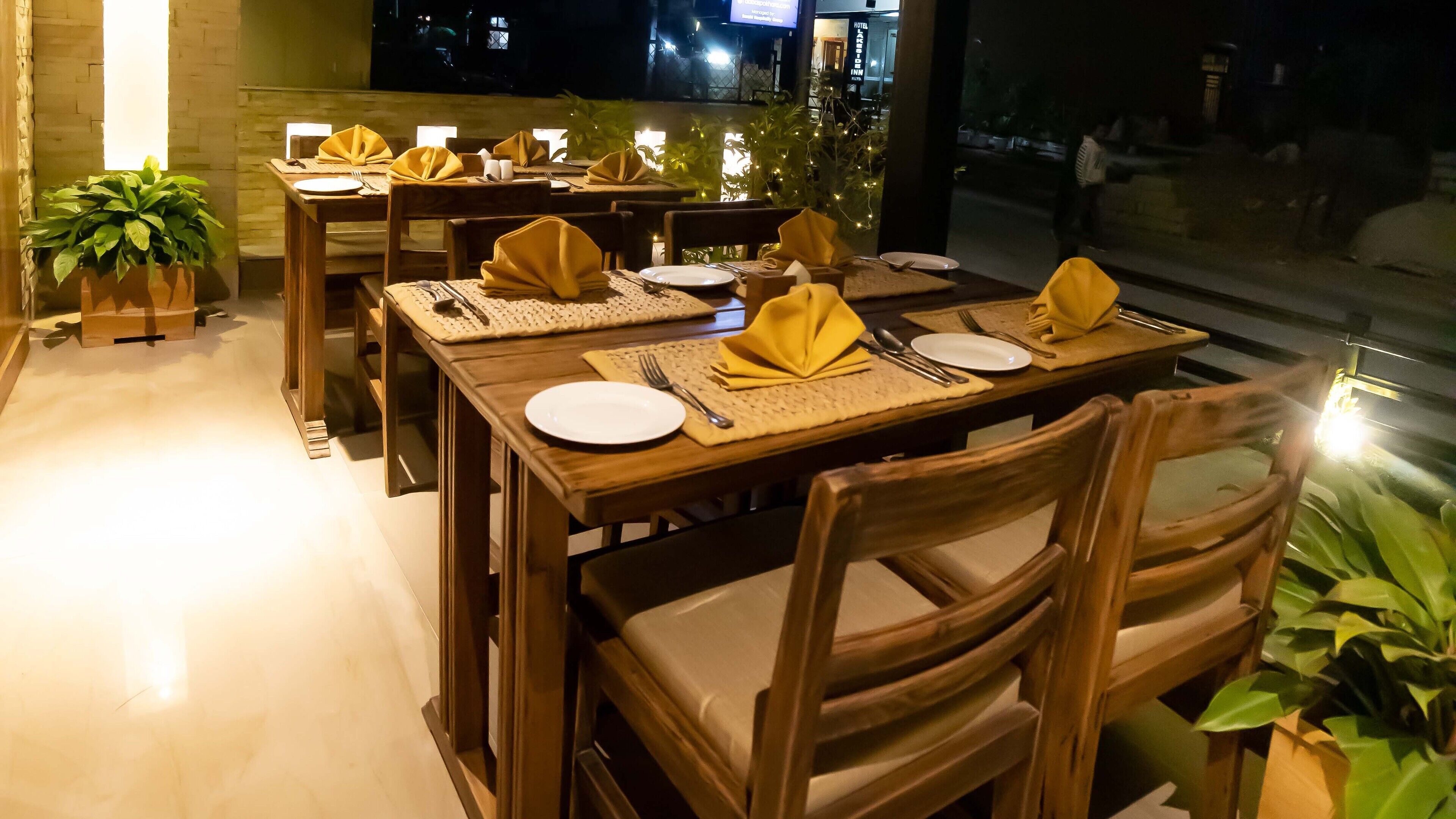A dining area with wooden tables and chairs, neatly set with plates, cutlery, and napkins.