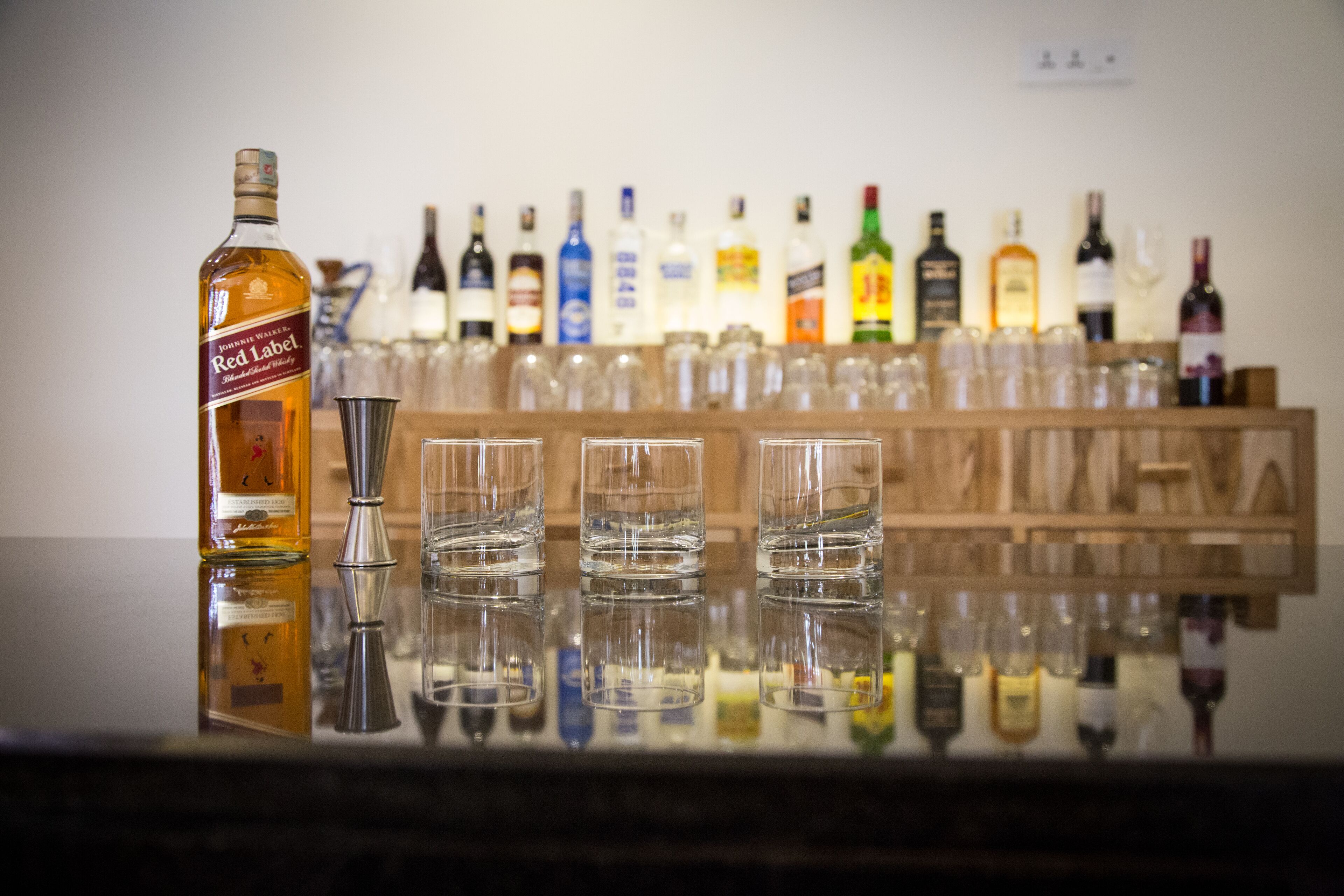 Un bar con una botella de whisky Red Label y varios vasos sobre una superficie reflectante.
