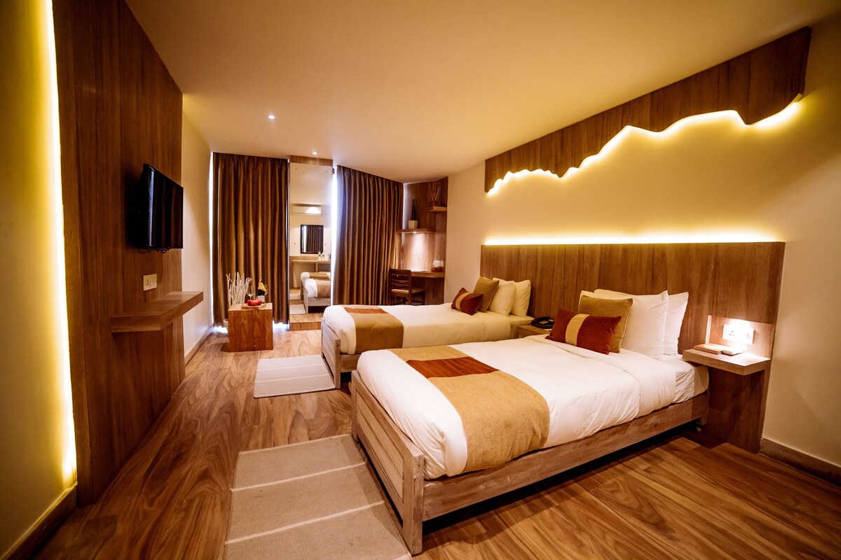 A hotel room with two beds, wooden flooring, a flat-screen TV, a bedside table, and a nightstand.