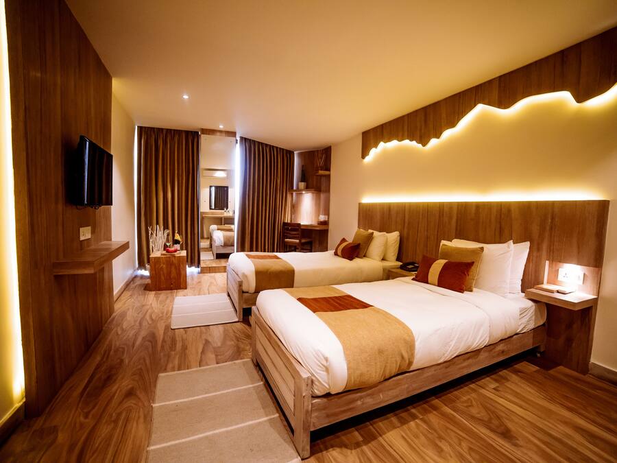 A hotel room with two beds, wooden flooring, a flat-screen TV, a bedside table, and a nightstand.