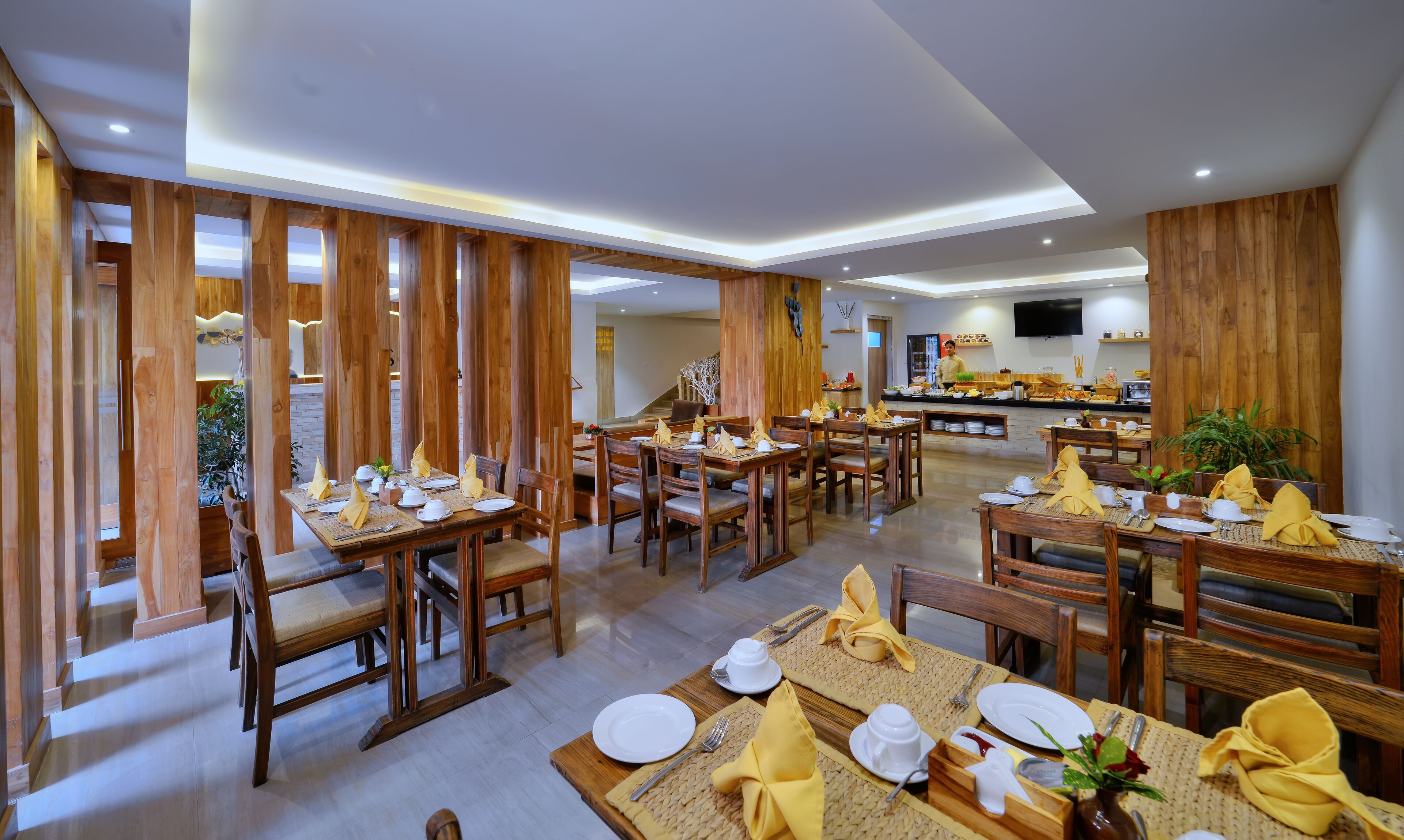 Un restaurante con decoración de madera, varias mesas dispuestas con servilletas amarillas, platos blancos y cubiertos.