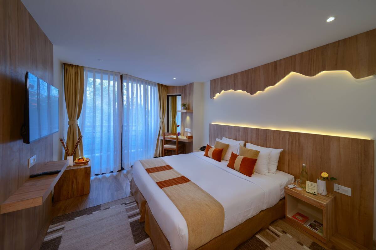 A modern hotel room with a large bed, bedside tables, a TV, and a view of the outdoors.