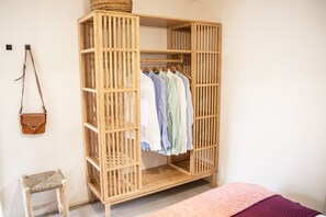 A wooden wardrobe with multiple shelves and hanging space, a small woven stool, and a pink bedspread. - StayatSas Tiny House Sam. Free WiFi, reserved parkingspace, kids & dogs welcome! (Epe)