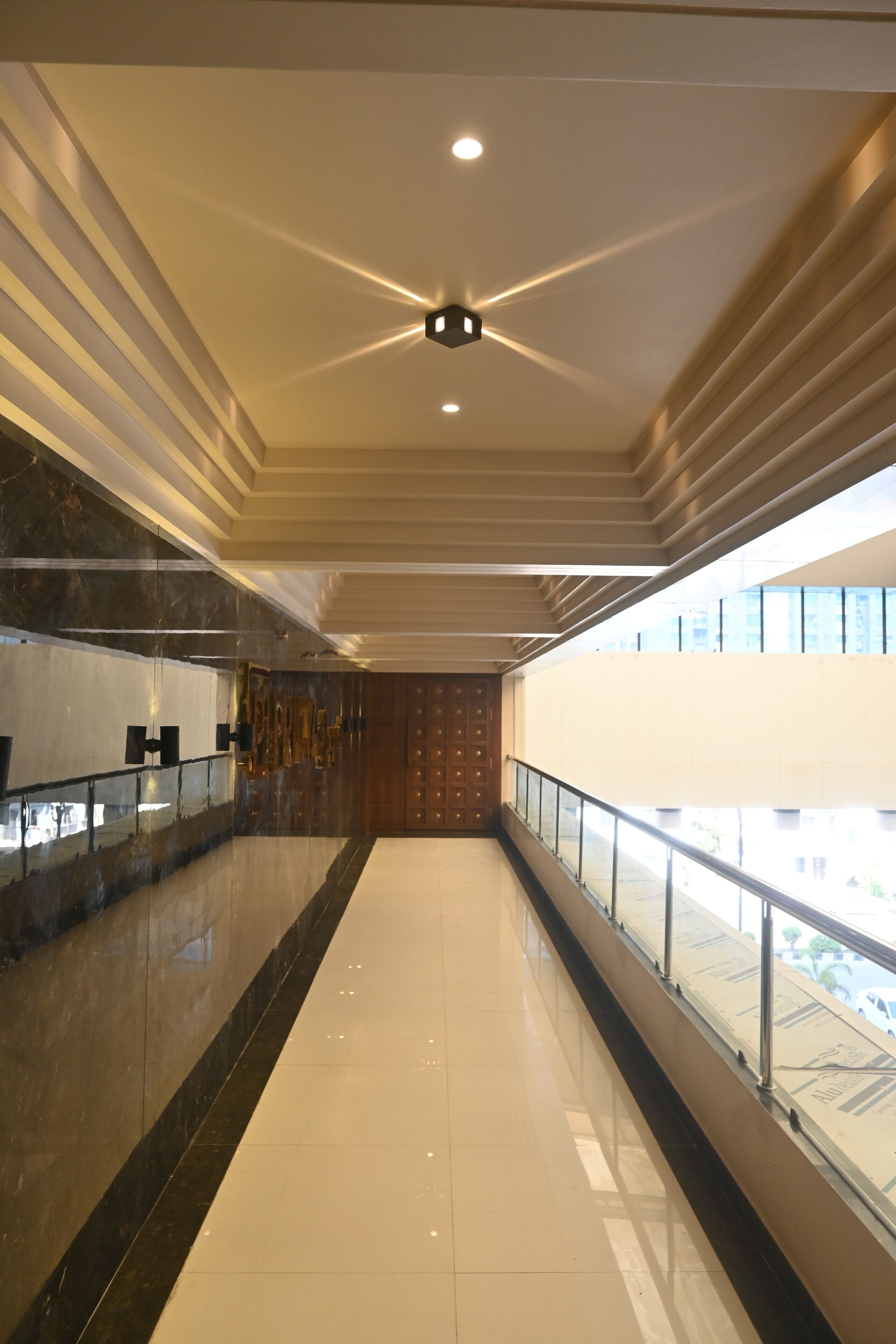 Un pasillo moderno de hotel con piso pulido, barandilla de vidrio e iluminación empotrada en el techo.
