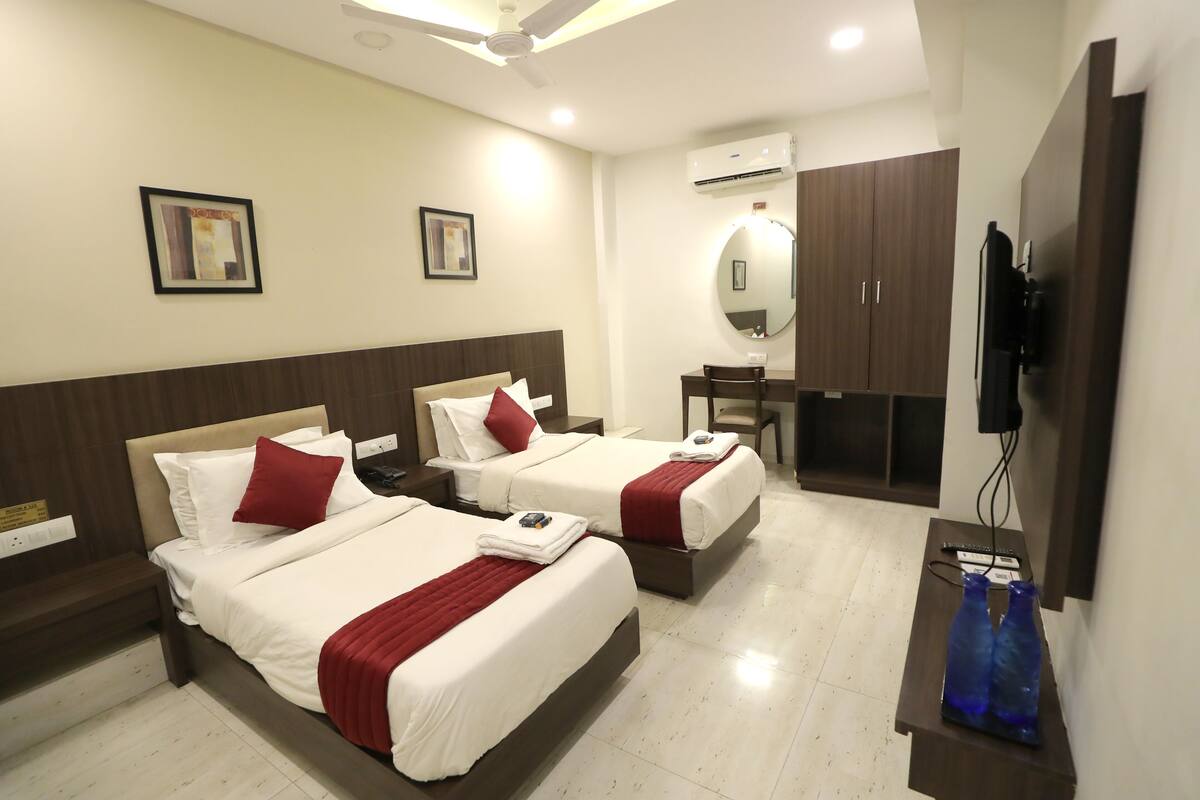 Une chambre d’hôtel avec deux lits, un bureau, une chaise, une télévision et un appareil de climatisation.