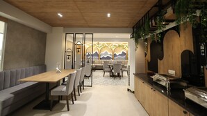 Een moderne eetruimte met een houten tafel, een grijze gestoffeerde bank en uitzicht op een berglandschap door een glazen wand.