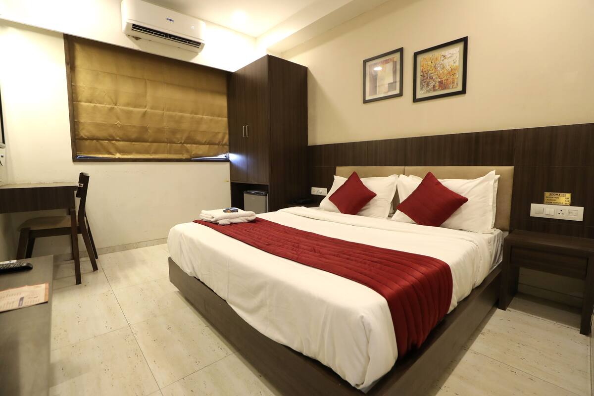 Une chambre d’hôtel avec un lit, un bureau, une chaise et une fenêtre avec un store.
