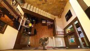 Un hall d’hôtel spacieux, doté d’un plancher en bois, d’un escalier central et d’un grand ventilateur.
