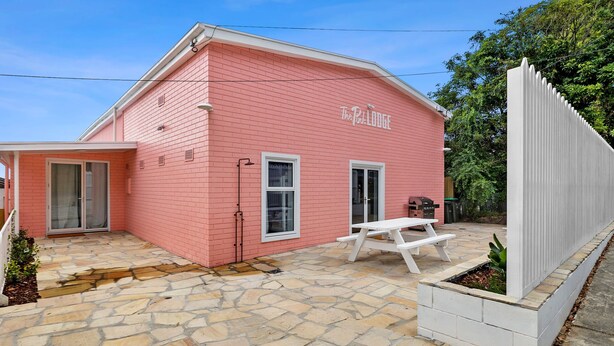 A pink building with a stone patio, a white picnic table, and a fenced area.