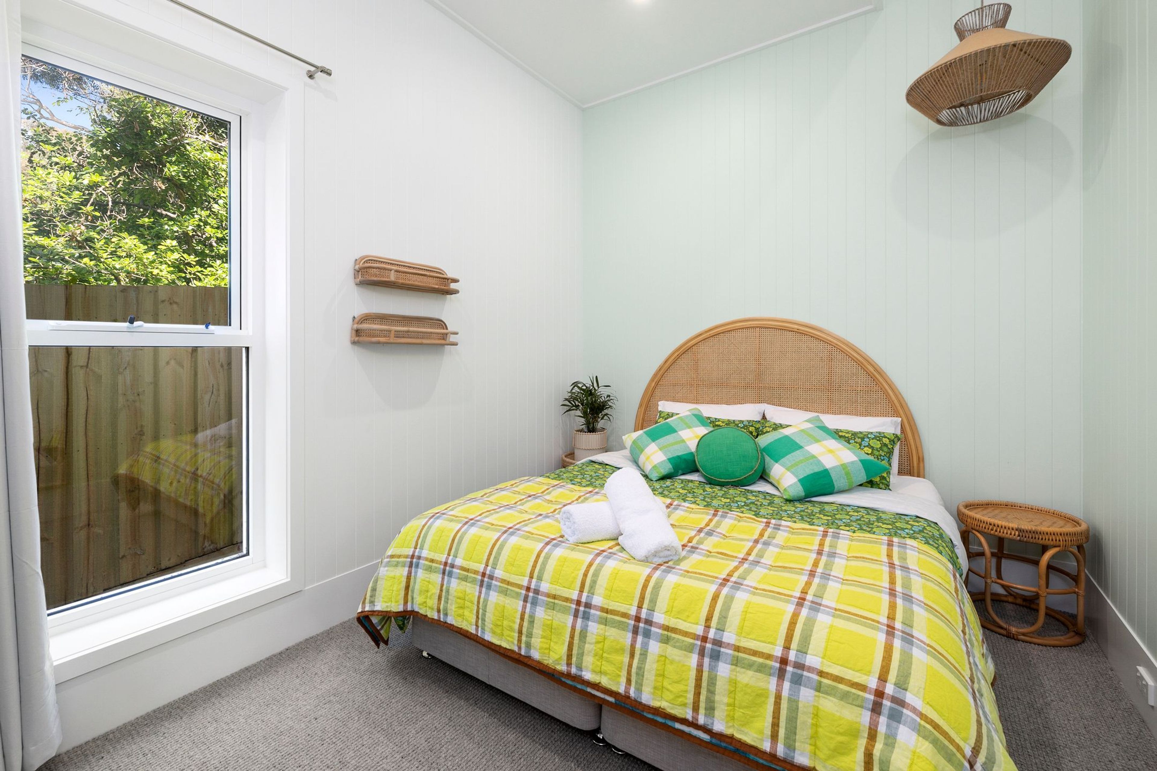 A bedroom with a bed, a window, a small stool, and a hanging light fixture.