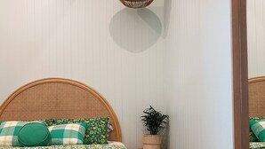 A bedroom with a large bed, a hanging light fixture, a small side table with a plant, and a mirror on the wall.