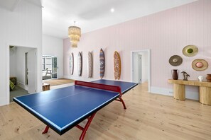 Habitació amb taula de ping-pong, sòl de fusta, paret rosa decorada amb uns surfboards i una làmpada al sostre.