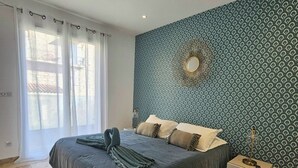 A bedroom with a bed, a nightstand, a mirror, and a patterned wall. - Spacious, bright apartment on the harbour for 4 to 6 people (Porto-Vecchio)