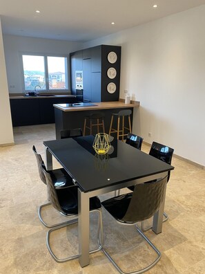 Une cuisine moderne avec des meubles de couleur sombre, une table à manger noire et une vue sur la ville grâce à de grandes fenêtres.
