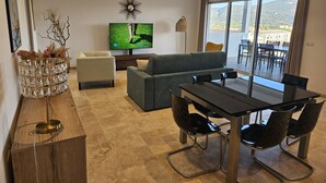 A modern living room with a sofa, a dining table with chairs, a TV, and a balcony with a view. - Spacious, bright apartment on the harbour for 4 to 6 people (Porto-Vecchio)