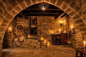 Um quarto com paredes de pedra, uma escadaria de madeira, um candelabro e arandelas.