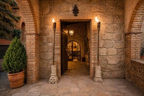 An arched stone entrance with two lit torches, a potted plant, and a lantern.